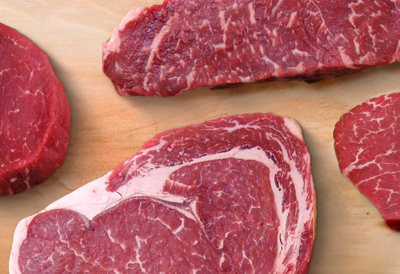 A close-up of assorted raw steaks on a cutting board.