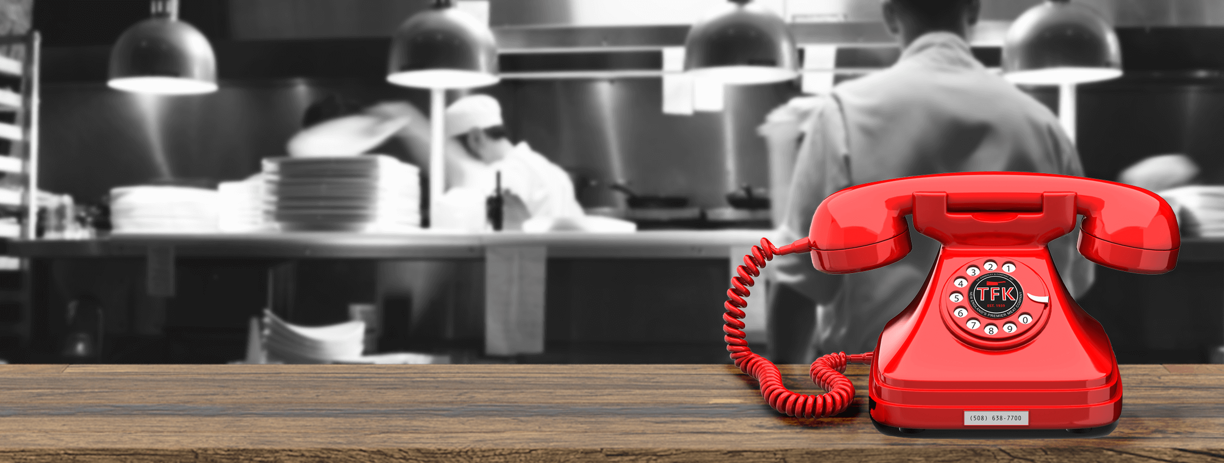 A red phone on a table in front of chefs working in the background.